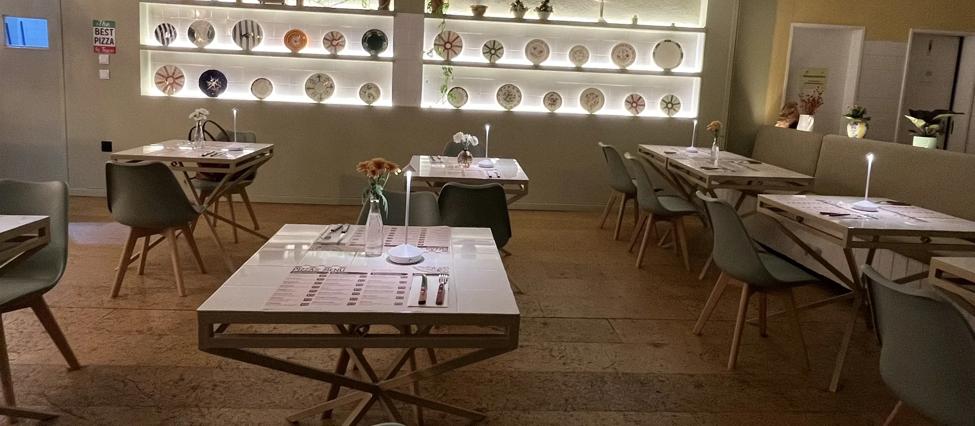 4 Projetos Comerciais Interior de restaurante com parede de pratos decorativos iluminada e mesas em tons claros — projeto comercial Vivenda Creative Home