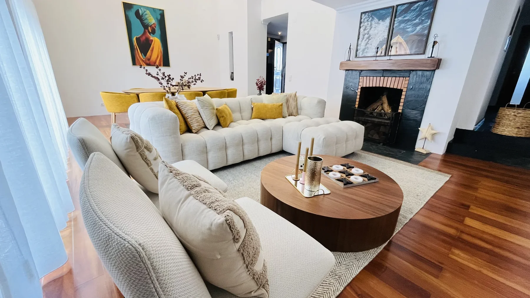 Quem Somos Sala de estar com sofás claros, mesa de centro em madeira, lareira em lousa negra e apontamentos amarelos — projeto Vivenda Creative Home em Lisboa